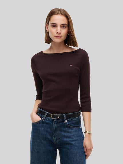 Frauenmodel trägt Slim Fit Langarmshirt aus reiner Baumwolle von Tommy Hilfiger in Dunkelbraun, kombiniert mit blauer Jeans, Nahaufnahme Oberkörper, Damen T-Shirt von Tommy Hilfiger.