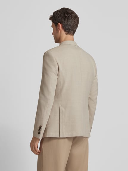 Männermodel trägt Slim Fit Sakko aus Schurwoll-Baumwoll-Mix Modell 'Heazy' von JOOP! Collection in Beige, feine Struktur, Ganzkörperansicht Rückansicht. Rückenlänge 73 cm, Schulterbreite 42 cm, Ärmellänge 63 cm, Zweireiher, Reverskragen, aufgesetzte Taschen.