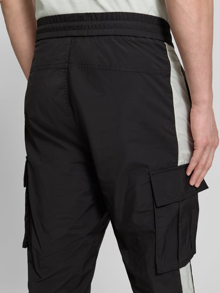 Männermodel trägt Regular Fit Cargohose mit Label-Applikation Modell 'COLAS262' von HUGO, Two-Tone-Optik, Twill, Nahaufnahme Rückansicht.