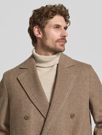 Männermodel trägt Mantel mit Reverskragen und Eingrifftaschen Modell 'NEKOLA' von DRYKORN im Baumwoll-Mix in Beige, Nahaufnahme Oberkörper.
