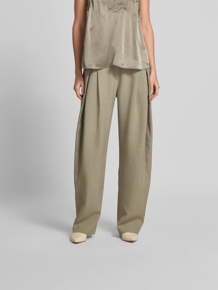 Frauenmodel trägt Wide Fit Stoffhose mit Bundfalten von Iro in Beige mit Eingrifftaschen, Gesäßtaschen, Haken- und Reißverschluss, Ganzkörperansicht von vorne.