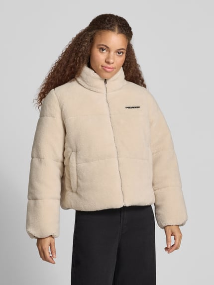 Kobiece model prezentuje Relaxed Fit kurtkę w imitacji futerka Model 'GEORGIA' od PEGADOR, kremowy kolor, detal z logo, stójka, zamek błyskawiczny, Długość tyłu w rozmiarze S: 57 cm, szerokość ramion w rozmiarze S: 41 cm, szerokość klatki piersiowej w rozmiarze S: 51 cm, długość rękawów w rozmiarze S: 63 cm, widok całej sylwetki z przodu.