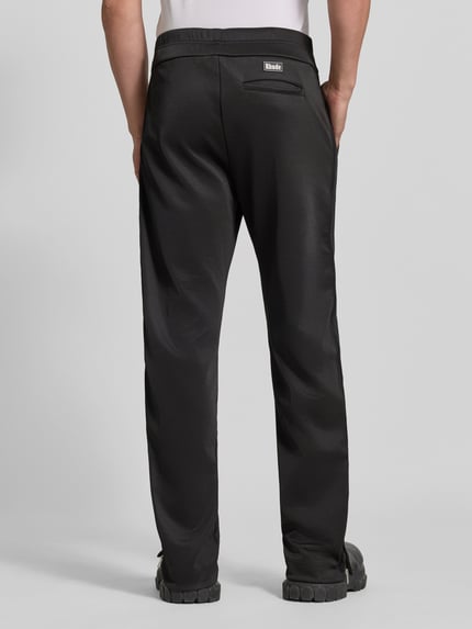 Männermodel trägt Sweatpants mit Stretch-Anteil von RHUDE in Schwarz, lockere Passform, Ziernähte, ausgestellter Beinabschluss, Ganzkörperansicht Rückansicht