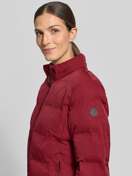 Frauenmodel trägt Steppjacke mit Kapuze Modell 'KAILA' von Cars Jeans in Dunkelrot, sichtbarer Reißverschluss und Eingrifftaschen, Nahaufnahme Oberkörper, Regular Fit, KI-modifiziertes Bild.