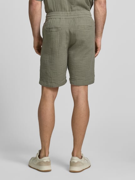 Männermodel trägt Shorts mit Eingrifftaschen und elastischem Bund von Lindbergh aus Reine Baumwolle in Loose-Fit, Rückansicht Ganzkörperansicht.