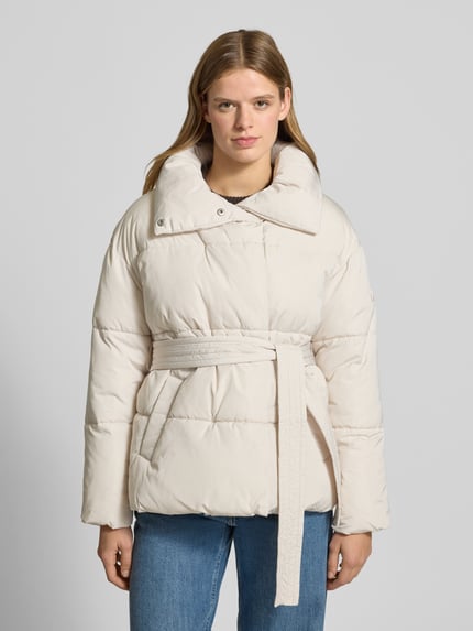 Vrouwenmodel draagt gewatteerd jack met opstaande kraag, steekzakken en strikceintuur, model 'Margitta' van LeGer by Lena Gercke, regular fit, kleur crème, textuur glad met doorgestikte naden, ruglengte 70 cm, schouderbreedte 57 cm, borstwijdte 58 cm, mouwlengte 55 cm, voorkant geheel zichtbaar, opname: totaalbeeld vooraanzicht.