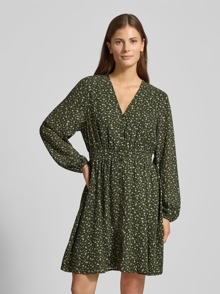 Frauenmodel trägt Minikleid im Allover-Look mit Knopfleiste Modell 'Kaylen Oceanna' von MSCH Copenhagen, dunkelgrün mit weißen Mustern, A-Linie, V-Ausschnitt, lange Ärmel, Ganzkörperansicht von vorne.