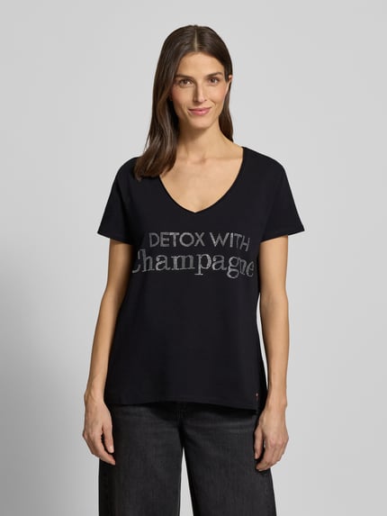 Frauenmodel trägt T-Shirt mit Label-Detail von miss goodlife, Baumwoll-Elasthan-Mix, lockerer Schnitt, V-Ausschnitt, schwarze Farbe, Ganzkörperansicht von vorne.
