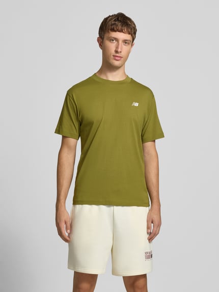 Männermodel trägt olivgrünes T-Shirt mit Label-Stitching Modell 'ESSENTIALS' von New Balance, Baumwolle, gerade Form, Ganzkörperansicht von vorne.