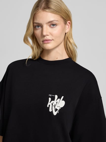 Modelka kobieca nosi Oversized T-Shirt mit Label-Print od Karo Kauer, czarna bawełna, okrągły dekolt, nadruk z przodu, zbliżenie na górną część ciała