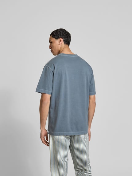 Männermodel trägt Regular Fit T-Shirt aus reiner Baumwolle von Closed in Blau mit Used-Look und Label-Print, Ganzkörperansicht Rückansicht.