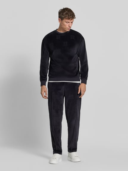 Männermodel trägt Regular Fit Sweathose mit Samtstruktur von HUGO, einfarbiges Design mit Struktur, Ganzkörperansicht von vorne.