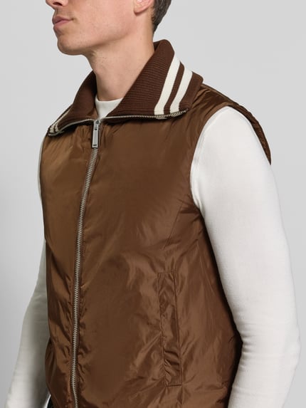 Männermodel trägt Weste mit Kontraststreifen von Dsquared2, braun mit weißem Ripp-Umlegekragen, Zweiwege-Reißverschluss, Nahaufnahme Oberkörper. Gerade Passform, elastischer Bund, sportlicher Look.