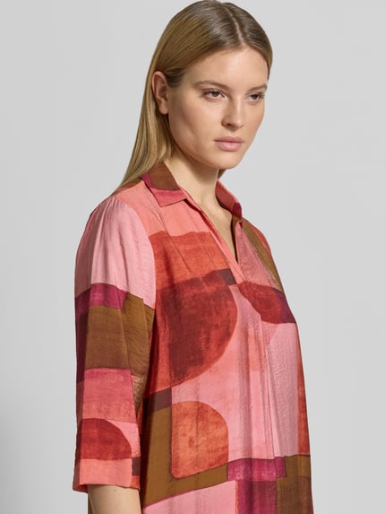 Frauenmodel trägt Relaxed Fit Midikleid aus Viskose-Mix Modell 'Catania' von Soyaconcept, buntes grafisches Muster, Halbarm, V-Ausschnitt, Umlegekragen, Nahaufnahme Oberkörper, Rückenlänge bei Größe S: 130 cm, Brustweite bei Größe S: 58 cm, Ärmellänge bei Größe S: 41 cm.
