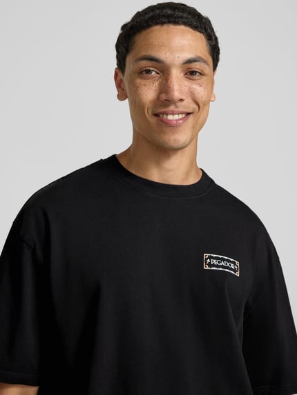 Männermodel trägt zwart oversized fit heren T-shirt van puur katoen, logoprint voor, model 'Viborg' van Pegador, nahaufnahme bovenlichaam.