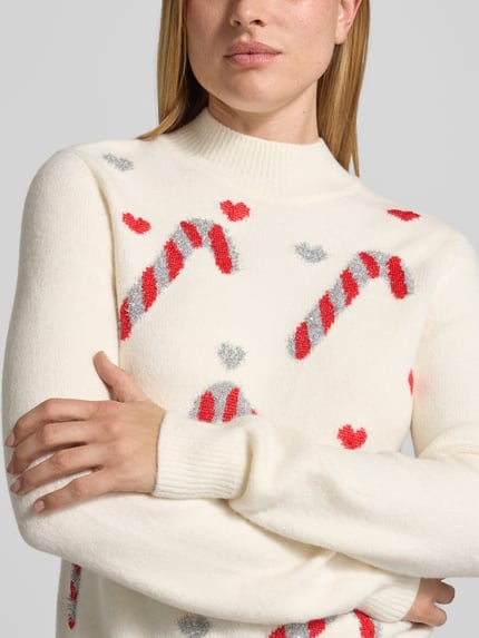 Frauenmodel trägt Strickpullover im Allover-Look mit Stehkragen von Christian Berg Woman, weiß mit roten und grauen Mustern, Material-Mix mit Stretch-Anteil, Nahaufnahme Oberkörper.