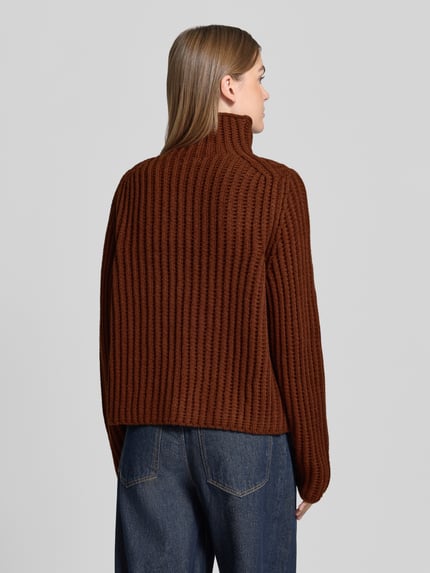 Frauenmodel trägt Strickpullover mit Stehkragen Modell 'ARWIE' von DRYKORN, braune Farbe, gerippte Textur, Rückenansicht, Ganzkörperansicht Rückansicht, Material-Mix mit Alpaka-Anteil, Regular Fit, Rückenlänge 57 cm, Ärmellänge 63 cm.