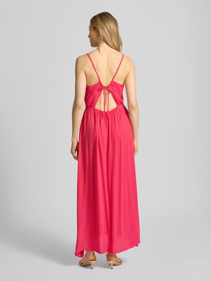 Frauenmodel trägt Midikleid aus Viskose mit tiefem Rückenausschnitt von ICHI, Taillierter Schnitt, Spaghettiträger, Modell 'MARRAKECH', leuchtendes Pink, fließende Textur, Ganzkörperansicht Rückansicht.