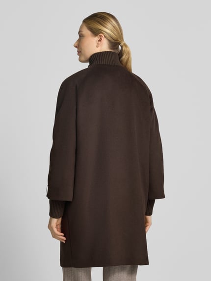 Frauenmodel trägt Mantel aus Woll-Mix mit gestricktem Stehkragen von COMMA in Dunkelbraun, strukturierte Oberfläche, Ganzkörperansicht Rückansicht. Straight Fit, Reiß- und Druckknopfverschluss, seitliche Eingrifftaschen, Woll-Mix mit Viskose, Rückenlänge 92 cm, Schulterbreite 40 cm, Brustweite 60 cm, Ärmellänge 63 cm.