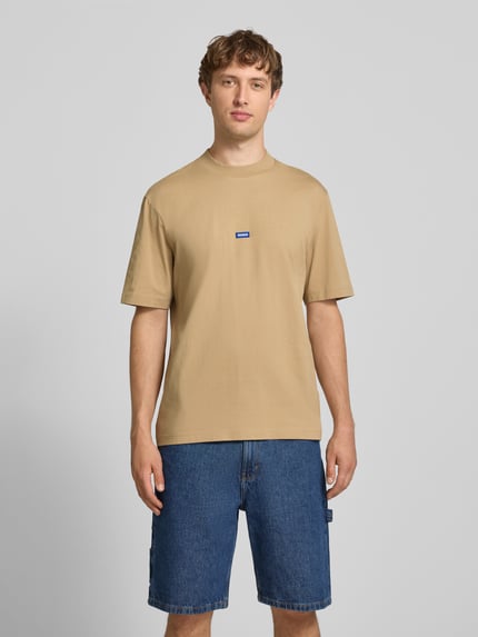 Mężczyzna nosi męski t-shirt Regular Fit T-Shirt aus reiner Baumwolle Modell 'NIEROS' od HUGO w beżowym kolorze, gładka faktura, jeansowe szorty. Ganzkörperansicht von vorne. Męski t-shirt HUGO Blue.