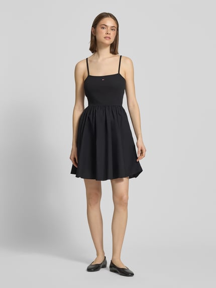 Frauenmodel trägt Tailliertes Freizeitkleid aus reiner Baumwolle von Tommy Jeans, unifarben in Schwarz, Mini-Länge, Logo-Stitching, Spaghettiträger, seitliche Eingrifftaschen, gerade Textur, U-Ausschnitt, Ganzkörperansicht von vorne.