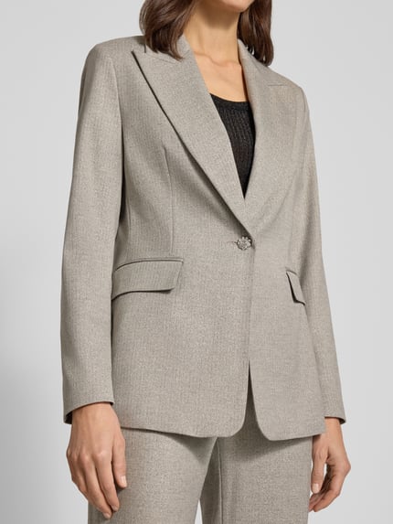 Frauenmodel trägt Slim Fit Longblazer aus Viskose-Mix von s.Oliver BLACK LABEL in Hellgrau mit Fischgrätmuster, Reverskragen, Pattentaschen, Knopf mit Strasssteinbesatz, Nahaufnahme Oberkörper.