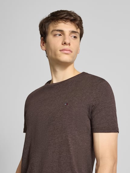 Männermodel trägt Regular Fit T-Shirt aus Baumwoll-Mix von Tommy Jeans in Braun, unifarben, Logo-Stitching, kurzarm, Nahaufnahme Oberkörper.