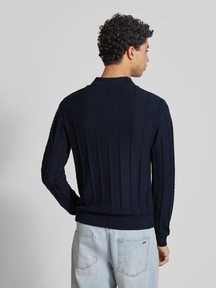 Męski model nosi Sweter z dzianiny z fakturowanym wzorem i kołnierzykiem polo od REVIEW, czarny, bawełna, krój slim fit, długość tyłu 65 cm, rękaw 66 cm, widok całej sylwetki z tyłu.