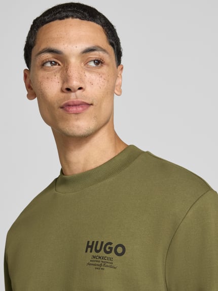 Mężczyznamodel nosi Regular Fit Sweatshirt aus reiner Baumwolle model 'Nespon' von HUGO, oliwkowy kolor, widoczne logo, Nahaufnahme górnej części ciała, Herren Sweatshirt von HUGO Blue.