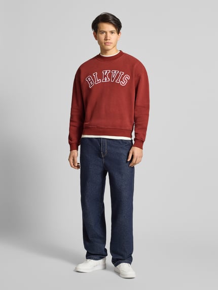 Männermodel trägt Sweatshirt mit Logo und Rundhalsausschnitt von BLKVIS in Bordeaux, reine Baumwolle, Relaxed Fit, Ganzkörperansicht von vorne.