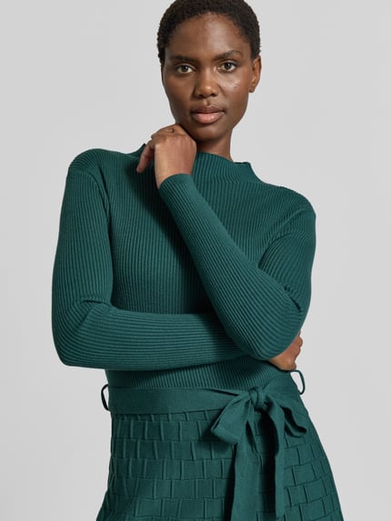 Kobiece model prezentuje Knielanges Strickkleid mit Bindegürtel od Apricot, Mieszanka wiskozy, Linia a, Długość do kolan, Stójka, wiązany pasek, Długość tyłu w rozmiarze S: 103 cm, Szerokość w rozmiarze S: 38 cm, Długość rękawów w rozmiarze S: 59 cm, zielony, tkanina o prążkowanej oraz plecionej fakturze, zbliżenie na górną część ciała.