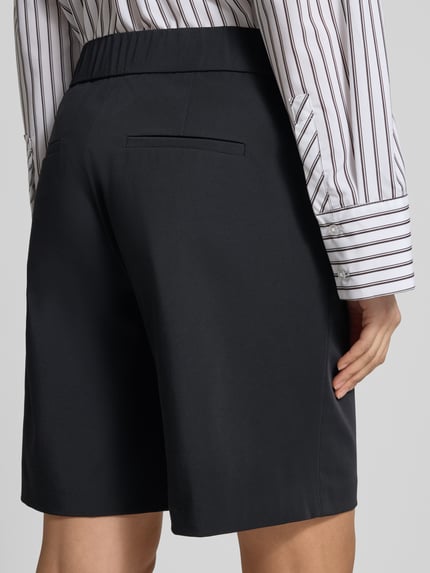Frauenmodel trägt Schlupfbermuda Techno Cotton Superstretch von Raffaello Rossi, Regular-Fit, Modell ISKA, Gesäßtaschen, Elastikbund, Farbe Schwarz, glatte Oberfläche, Kontext: Damen Schlupfbermuda, Bundweite 39 cm, Innenbeinlänge 24 cm, Ganzkörperansicht Rückansicht.