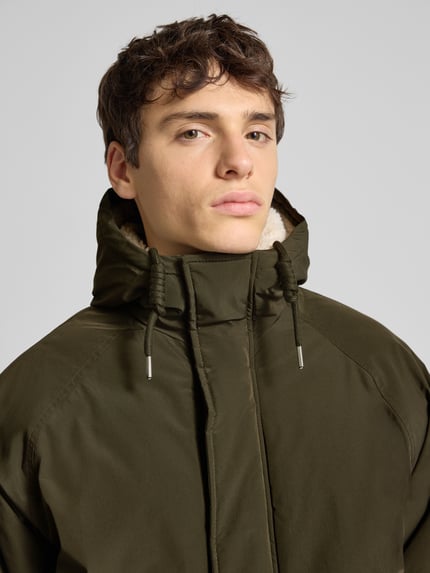 Männermodel trägt Parka mit Kapuze Modell 'WOOD' von Jack & Jones in Olivgrün, Reißverschluss und Tunnelzug, Nahaufnahme Oberkörper.