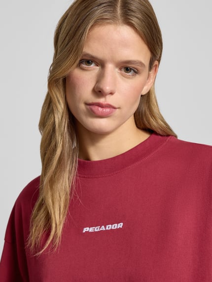 Frauenmodel trägt Oversized T-Shirt mit Logo Modell 'BRACY' von Pegador in Dunkelrot mit Rundhalsausschnitt, reine Baumwolle, Nahaufnahme Oberkörper.
