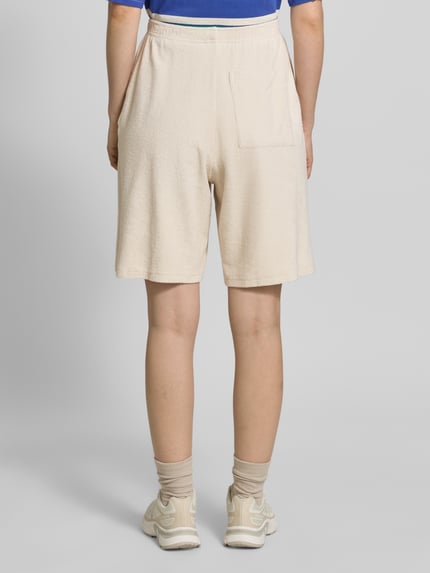 Frauenmodel trägt Sweatshorts mit Eingrifftaschen und Logo-Stitching Modell 'FUXOW' von American Vintage in Beige, Baumwolle, lockerer Schnitt, elastischer Bund, französische Eingrifftaschen, Rückansicht Ganzkörperansicht.