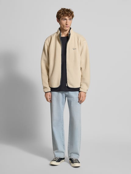 Männermodel trägt Teddyjacke mit Reißverschluss von Pegador in Beige mit Stehkragen, Regular Fit, Label-Stitching, Ganzkörperansicht von vorne.