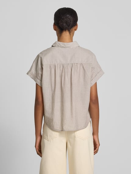 Vrouwenmodel draagt Boxy Fit Hemdbluse aus reiner Baumwolle van Marc O'Polo met all-over motief in beige en wit, achterpas met plooien, borstzakken, boxy fit, puur katoen, gestreept patroon, overhemdkraag, korte mouw met vaste omslag, ganzlichaamsaanzicht achteraan.
