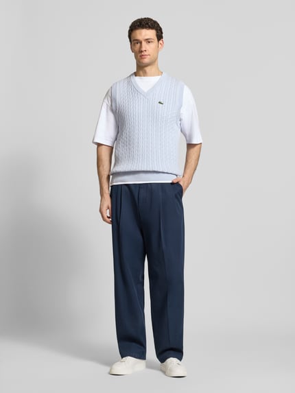 Männermodel trägt Regular Fit Pullunder aus Baumwoll-Mix von Lacoste in Hellblau mit Zopfmuster, unifarben, Strickoptik, Logo-Detail, Ganzkörperansicht von vorne.