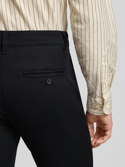 Männermodel trägt Slim Fit Stoffhose aus Viskose-Mix Modell 'MARK' von Only & Sons, schwarzer Anzug-Stoff, Detailaufnahme Rückansicht, Eingrifftaschen, Knopfverschluss, Viskose-Elasthan-Mix, Kontext: Bundweite 43 cm, Innenbeinlänge 78 cm bei Größe 32/32.