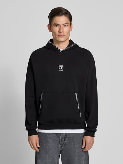 Męski model nosi Regular Fit Hoodie aus reiner Baumwolle Modell 'DAROHOOD' von HUGO, czarny, kangurka, długi rękaw, krój regular fit, haftowane logo, tekstura sweat, widok całej sylwetki z przodu.