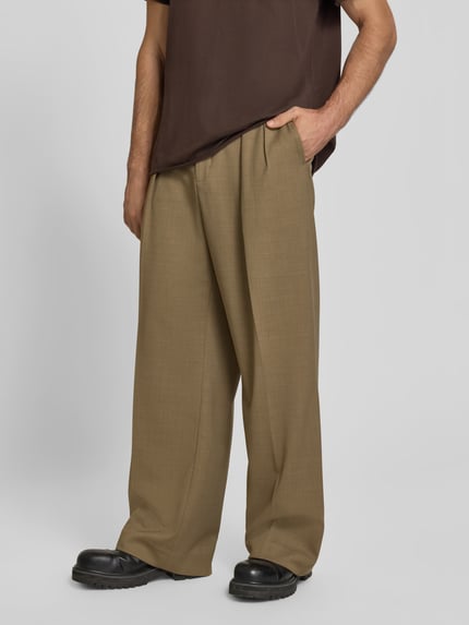 Männermodel trägt Wide Fit Stoffhose aus Woll-Mix von Filippa K in Beige mit Kellerfalten, Nahaufnahme Oberkörper, Produktdetails sichtbar.