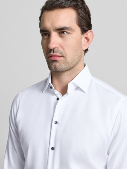 Männermodel trägt Regular Fit Business Hemd aus Baumwolle mit Kentkragen von Christian Berg Men, weiße Textur, Nahaufnahme Oberkörper.