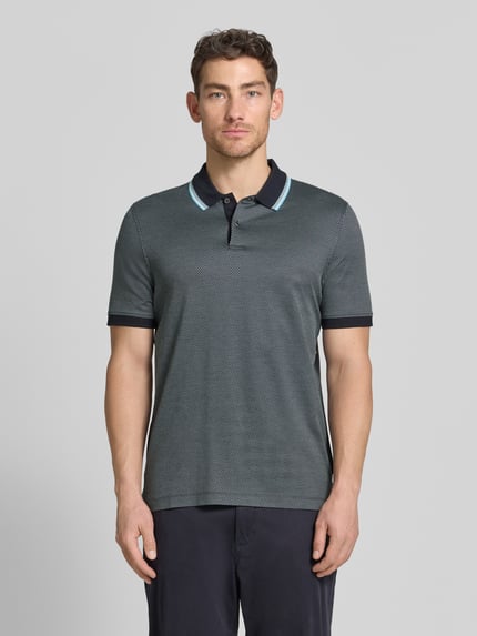 Męski model nosi Regular Fit Poloshirt mit Polokragen und kurzer Knopfleiste von bugatti, bawełna, detal z logo, długość tyłu 70 cm, krój regular fit, widok całej sylwetki z przodu.