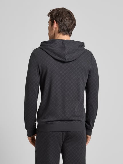 Männermodel trägt Sweatjacke mit Logo-Muster und Kapuze von JOOP! Collection aus pure katoen, regular fit, rugzakzicht, egale zwarte kleur, textuur met logo patroon, rugaanzicht.