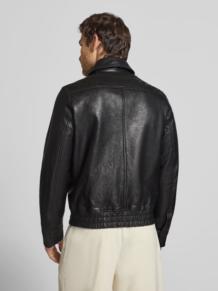 Männermodel trägt Lederjacke aus Schafsleder mit Pattentaschen von Paul Smith, Bomber Fit, glatte schwarze Textur, Ganzkörperansicht Rückansicht.
