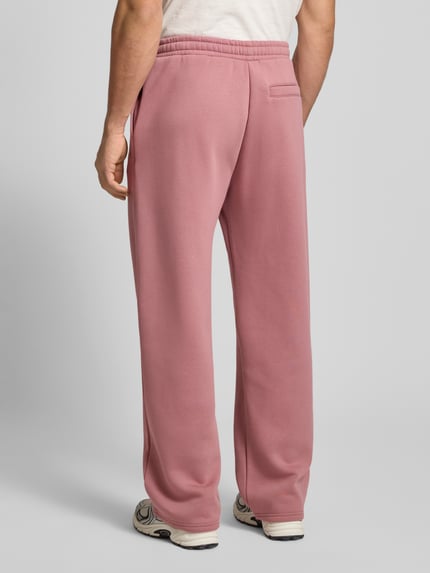 Männermodel trägt Loose Fit Sweatpants mit Seitentaschen von REVIEW, roze katoenmix, elastische taille, zijzakken, achterzak, Ganzkörperansicht Rückansicht.