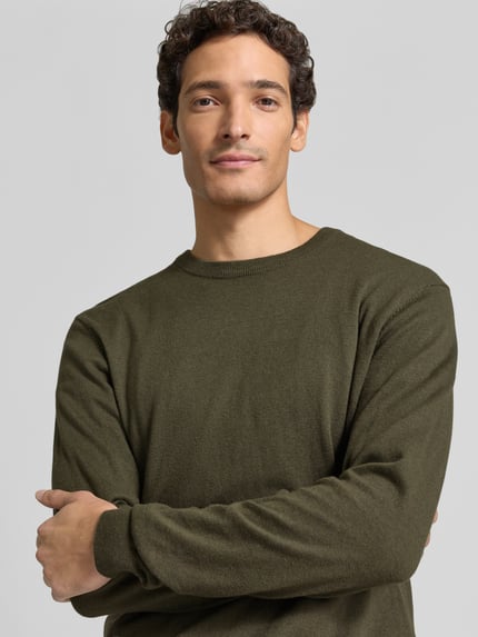Mężczyzna nosi Regular Fit Strickpullover aus Baumwoll-Mix mit Kaschmir-Anteil od Casual Friday, kolor oliwkowy, faktura dzianiny, długie rękawy, ściągacze, okrągły dekolt, emblemat marki, widok z przodu, zbliżenie na górną część ciała.