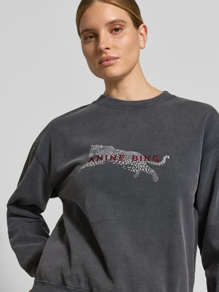 Frauenmodel trägt Oversized Sweatshirt aus reiner Baumwoll von Anine Bing in Dunkelgrau mit Motiv-Print und Label-Detail, Nahaufnahme Oberkörper.