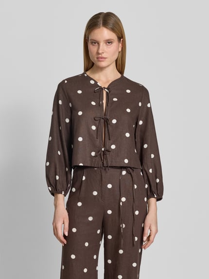 Frauenmodel trägt Regular Fit Bluse mit Zierschleifen von Jake*s Casual, braun mit weißen Punkten, Leinen-Viskose-Mix, Rundhalsausschnitt, eingefasste Ärmelabschlüsse, langärmeliges Design, Ganzkörperansicht von vorne.