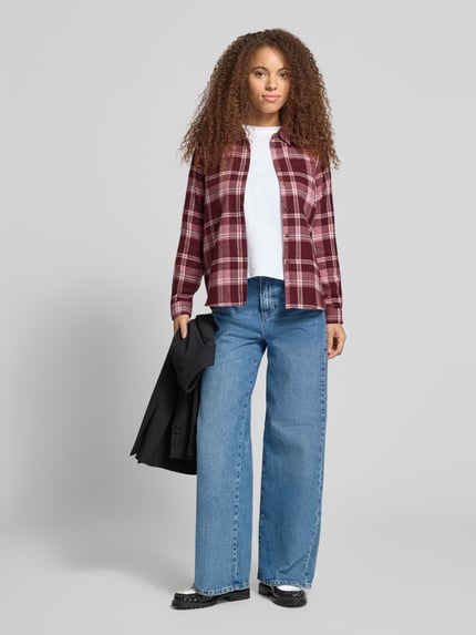 Frauenmodel trägt Longline Hemdbluse mit Label-Detail von ONLY, karierter Stoff in Rot und Weiß, kombiniert mit blauer Jeans, Ganzkörperansicht von vorne, Damen Hemdbluse von ONLY